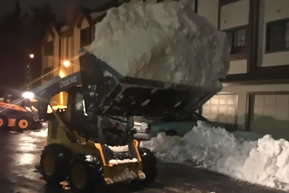 A skid steer from Absolute Tree lifting snow during at night in Alexandria, VA.